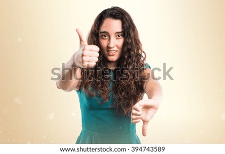 Teenager girl making good-bad sign over ocher background