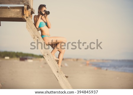 Happy woman photographer on vacation shooting.Photographer ready to take sea landscape pictures with dslr camera on the beach.Professional travel photography.Summer memories.Capturing moment of life