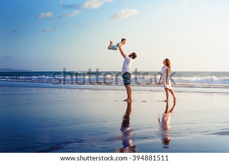 Happy family - father, mother, baby son walk with fun along edge of sunset sea surf on black sand beach. Active parents and people outdoor activity on summer vacations with children on Bali island
 Royalty-Free Stock Photo #394881511