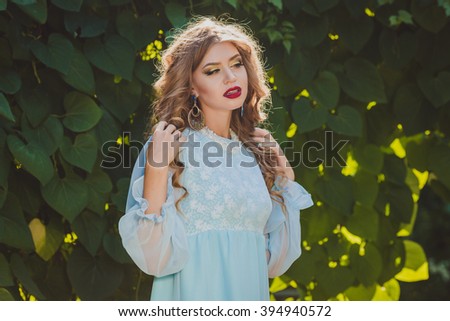Beautiful young girl in blue dress near the tree in the  garden