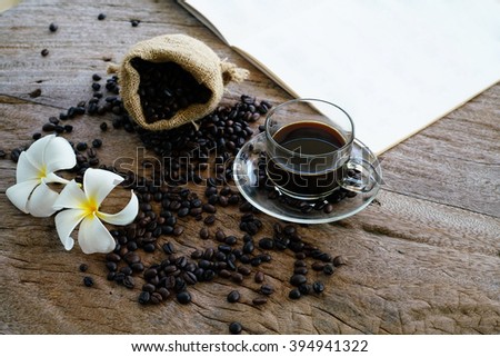 A sack of coffee beans, a cup of coffee, a book of music note and some flower on the stripe wooden background (Selective focus on cup of coffee)