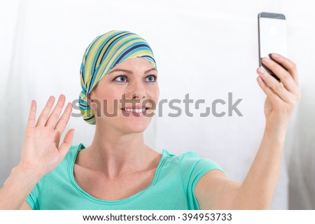 woman, bald from chemotherapy, doing a selfie with cell phone  