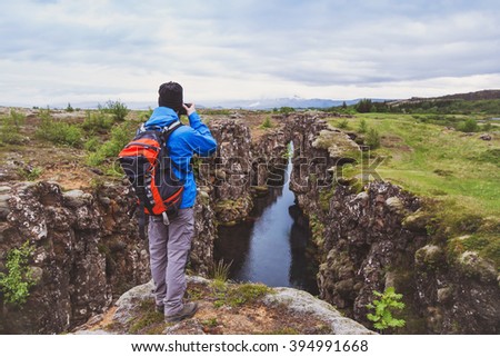 nature photographer, hiker with backpack taking photo of beautiful landscape in Iceland national park Thingvellir