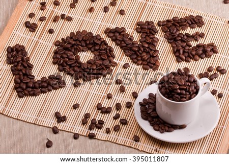 Coffee beans are laid out on a table on a straw or wooden stand. Coffee is laid out in the shape of a LOVE. Good for Valentine's day, at the time of declaration of love, makes an offer