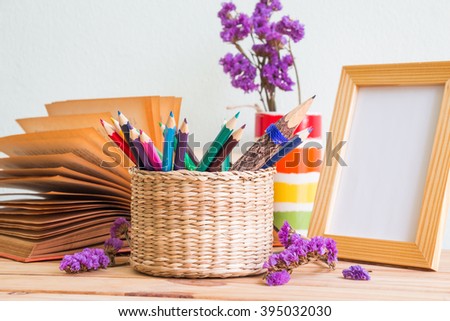 Pencils and colored pencils in the basket, open book, purple flowers in a vase and wooden photo frame on a wooden table, selective focus