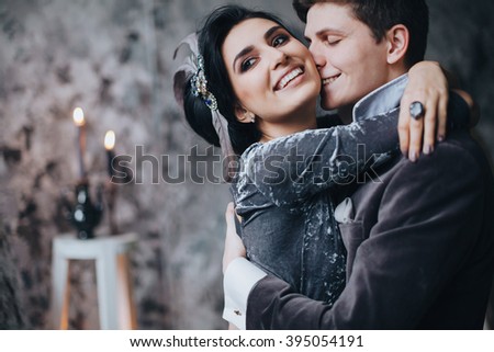 Wedding. Decor. Newlyweds. Artwork. Bride in a gray dress and groom in a suit standing on the background of textured gray wall, chair and easel