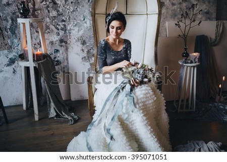 Wedding. Decor. Bride. The bride's bouquet. Artwork. Bride in blue and white dress sitting in a ? chair on a background of a gray textured wall and holding a bouquet of flowers and greenery