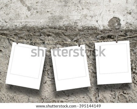 Close-up of three hanged blank square instant photo frames with pegs against rough wall background