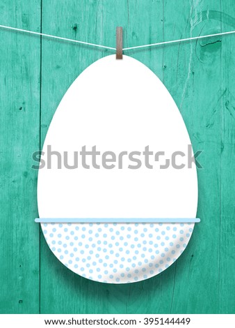 Close-up of one hanged decorated blank Easter egg frame with peg against aqua wooden boards background