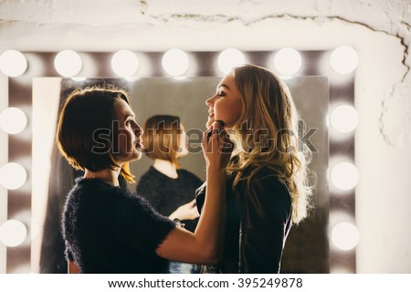 Young women doing makeup , old-fashioned. Stands near  mirror. Backstage.