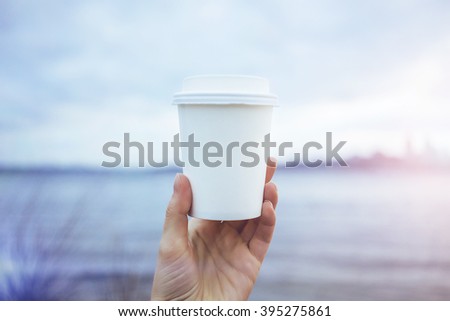 Hand holding paper cup of coffee on natural morning background. Film effect.