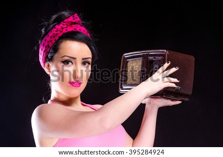 Pin-up style young woman holding a vintage radio against a black background