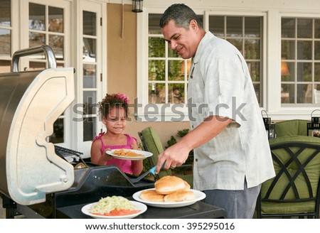 Father and daughter on patio grilling barbecue food smiling