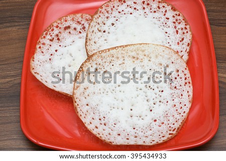 Top view Appam / Palappam made of rice, coconut, popular and traditional Kerala breakfast bread with beef curry/ Mutton curry/ meat curry. Kerala cuisine served on a bright red plate, India.