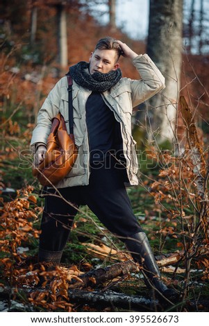 young guy in a jacket with a scarf on the neck, trousers and rubber boots walks alone in the Carpathian mountains with a backpack on his shoulders