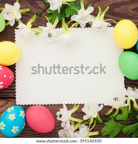 Easter. Festive composition of brightly colored Easter eggs, spring flowers and empty label to stick on  wooden desk.