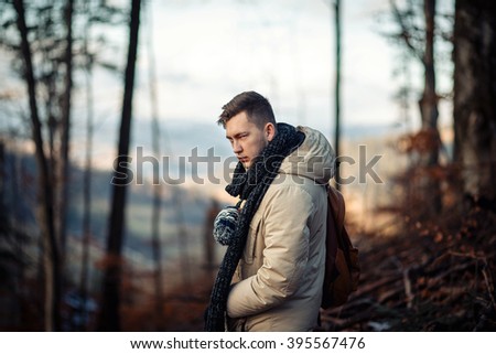 young guy in a warm cap and a jacket with a scarf on the neck, trousers and rubber boots walks alone in the Carpathian mountains with a backpack on his shoulders