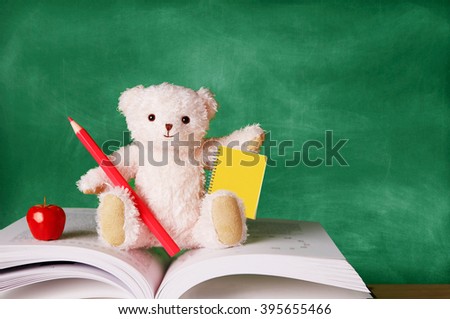 Cute teddy bear with a pencil,notebook,and apple sitting on the book in front of the blackboard. Kids study,school, education image.
    