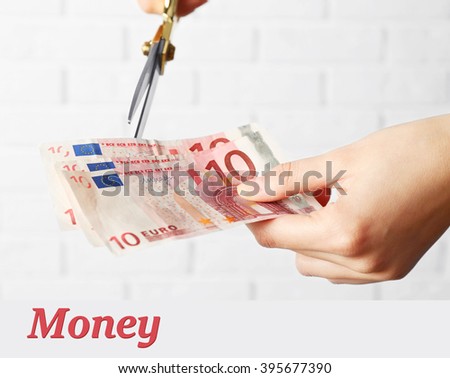 Hands with scissors cutting money on white brick wall background