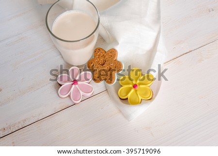 Glass of milk with cookies. Flower shaped colorful cookies on white wooden background
