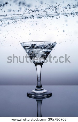 Ice in glass with water splash on blue background on table with refllection