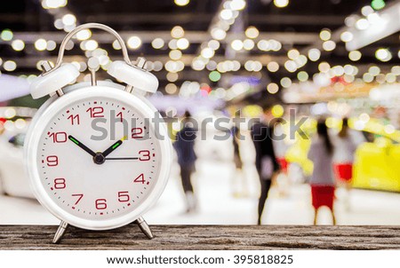 White alarm clock on the wooden with blurring of people background soft focus.