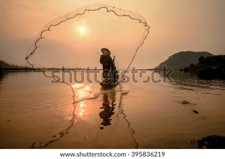 Silhouette of a fisherman throwing his net with sunset.