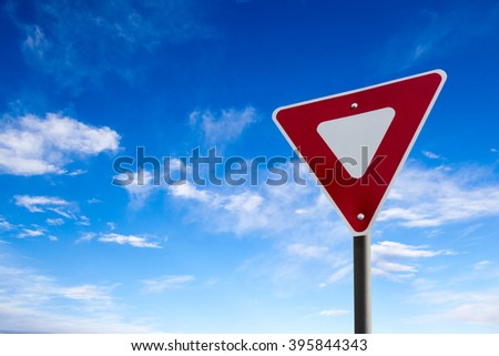 Conceptual yield sign against a blue cloudy sky.