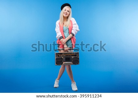 Full length portrait of a happy female teenager holding retro boom box on blue background