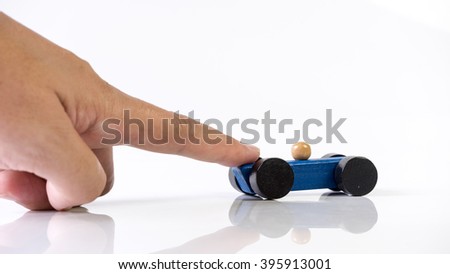 Hand playing with blue wooden toy race car on white empty background. Concept of dream car ownership and financing. Slightly de-focused and close-up shot. Copy space.
