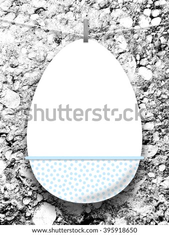 Close-up of one hanged decorated blank Easter egg frame with peg against black and white stone wall background