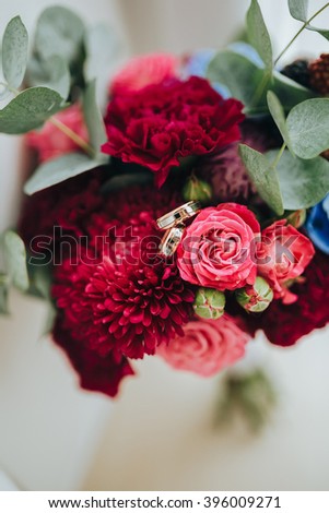 Wedding. The bride's bouquet. Bridal bouquet. Bouquet of red, pink, blue flowers, and greenery stands near a large window. Wedding rings lie on a bouquet