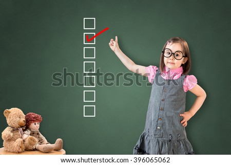 Cute little girl wearing business dress and checking on checklist box on green chalk board.