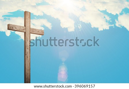 Old brown wooden cross, with sun flash on clouds background
