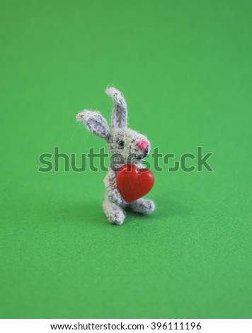 Cute funny gray little knitted rabbit with a small red heart in its paws. 
Symbol of the new year. Photo for a postcard.