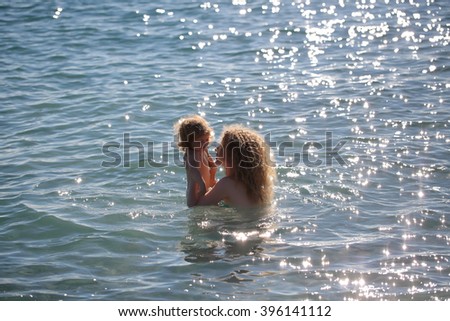 Young mother in bikini standing swimming and playing with male child boy in sea or ocean water sunny day outdoor on natural background, horizontal picture