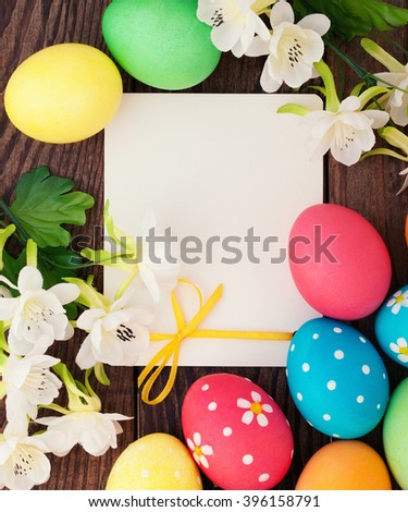 Easter. Festive composition of brightly colored Easter eggs, spring flowers and empty label to stick on  wooden desk.