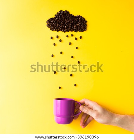 Coffee beans in shape of rainy cloud with purple cup on yellow background. Weather concept.