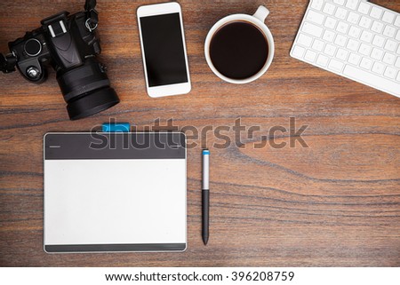 Wooden desk with a pen tablet, a dslr and a smartphone seen from above