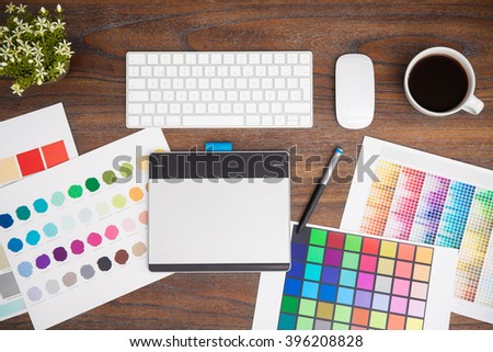 Top view of the workspace of a graphic designer, including some color swatches, a pen tablet, a keyboard and some coffee