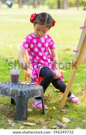 Littel asian girl painting with easel in garden