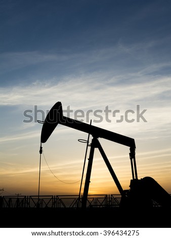 Cloudy sunset and silhouette of crude oil pump in oil field 