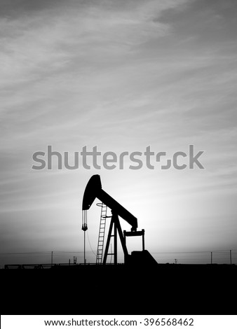 Cloudy sunset and silhouette of crude oil pump in oil field - black and white