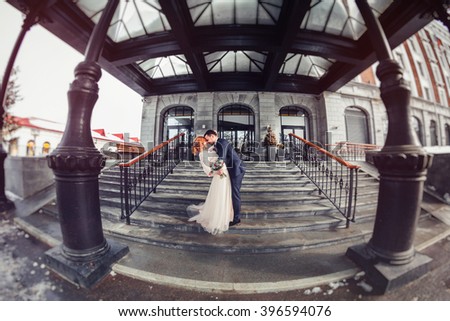 Bride and groom walking in the city. The picture on the wide-angle fisheye lens on the background of the modern hotel