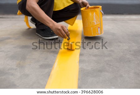 Man painting the yellow line on the concrete floor at car park