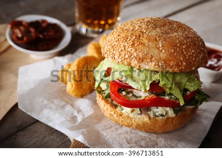 Big tasty hamburger with snacks and glass mug of light beer on wooden table
