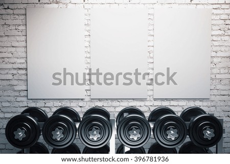 Row of dumbbells and three blank posters on brick wall background. Mock up