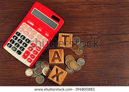 Word tax with coins and calculator on wooden table, top view