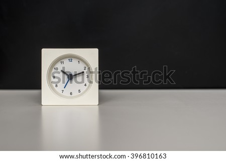 white clock on a white table against the background of black board.