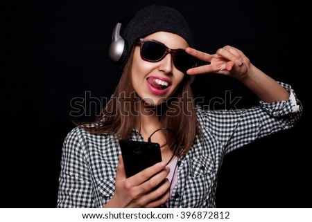 beautiful girl happy listening to music with big headphones with a phone or player, knit cap, photo studio, portrait of a woman on black background